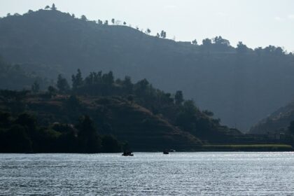 Image of lake surrounded by lush green hills and people on boat ride - Places to Visit Near Panchkula